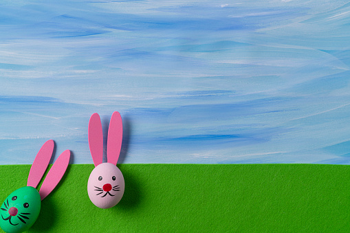 Painted easter eggs with easter bunny face on green felt and watercolor blue color sky
