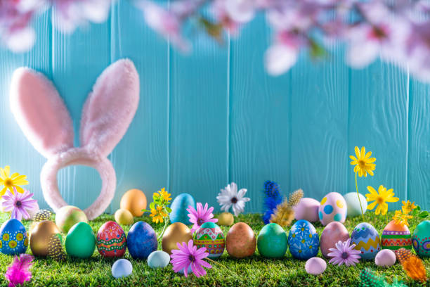 istock Easter eggs on turf grass and blue wooden wall with spring flowers 1369188015