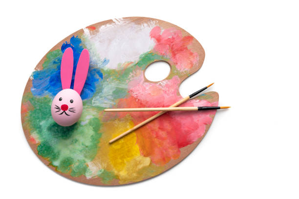 Easter Egg hand painted with bunny face and ears on painting palette isolated on white background