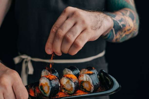 Chef with a tattoo on his arm sprinkles the rolls with spices. stock photo
