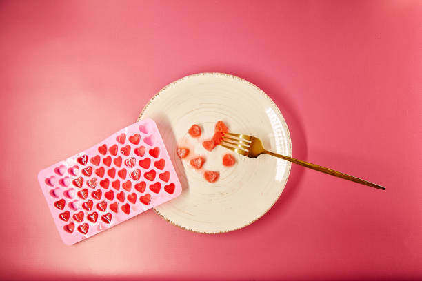 istock Cute frozen ice hearts on white plate with fork. Creative romantic dinner, Valentines Day concept. Pink gradient background. Top view 1369189979