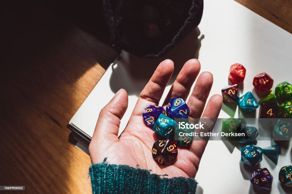 A hand holding various-shaped RPG dice Image of a hand holding various colored and shaped role-playing dice lit by sunlight Board Game Stock Photo
