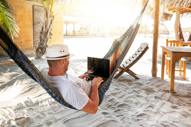 man with hat uses laptop remotely at the beach, near cabin. Playa La Ventanilla man with hat uses laptop remotely at the beach, near cabin. Playa La Ventanilla beach hut stock pictures, royalty-free photos & images