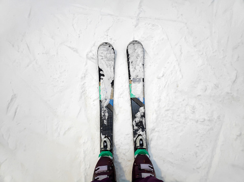 top above view of female womens legs in skis on white icy snow surface, mountain track background, skier legs on downhill start straight line rows ski slope piste. Winter active sport outdoor concept.