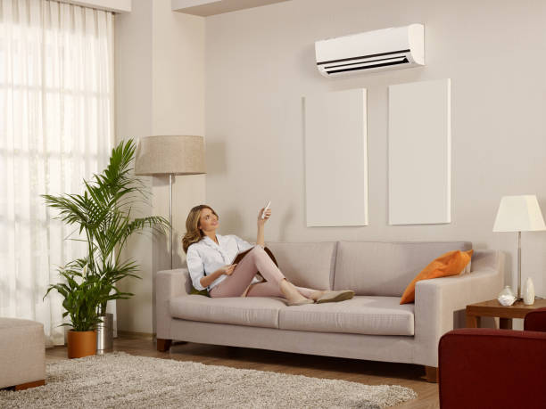 Resting in a room with air conditioner Young woman sitting and using remote control to control air conditioner in the house adjusting seat stock pictures, royalty-free photos & images