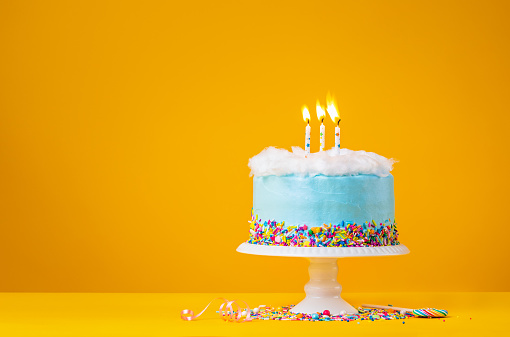 Blue Birthday cake with three  Birthday candles and candy sprinkles over a yellow background.