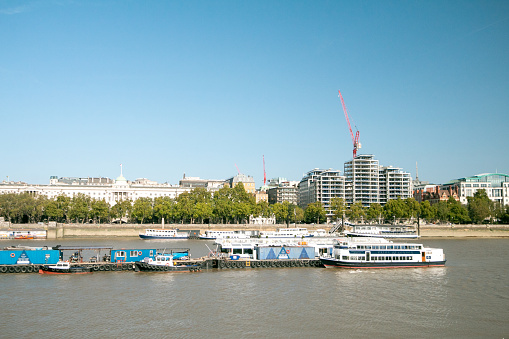 Victoria Embankment on River Thames in City of Westminster, London. Boats and barges are in the foreground and Somerset House is in the background.