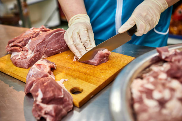 istock Cook cutting raw pork meat on wooden board in kitchen 1369201918
