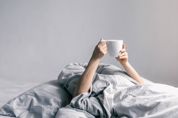 istock A woman's hand holds a cup of coffee while lying in bed. 1369203512