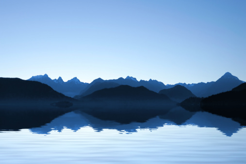 Wide view of ripples in an alpine lake with trees and mountains in the background.