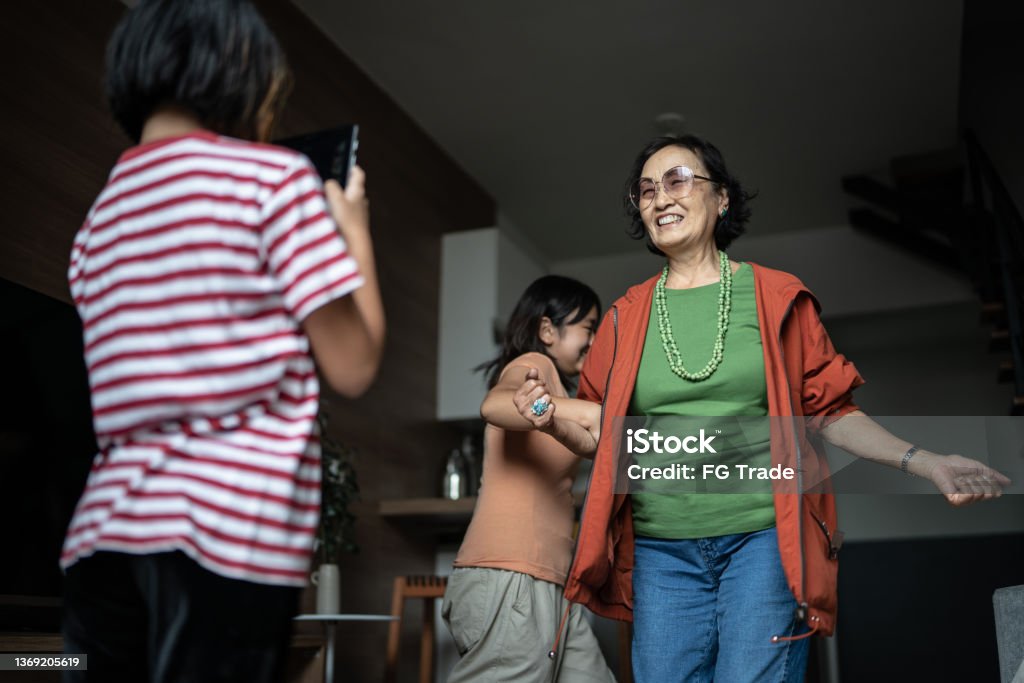 Girl filming sister and grandmother dancing at home Teenager Stock Photo