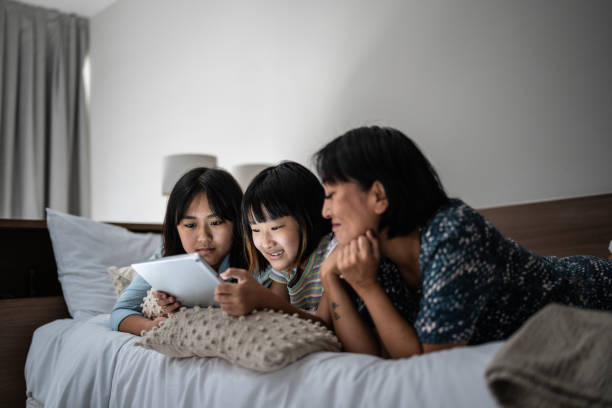 Mother and kids watching a movie on the digital tablet on the bed at home Mother and kids watching a movie on the digital tablet on the bed at home asian kids watching tv stock pictures, royalty-free photos & images