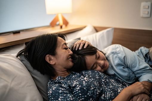 Mother laying down with daughter in bed at home