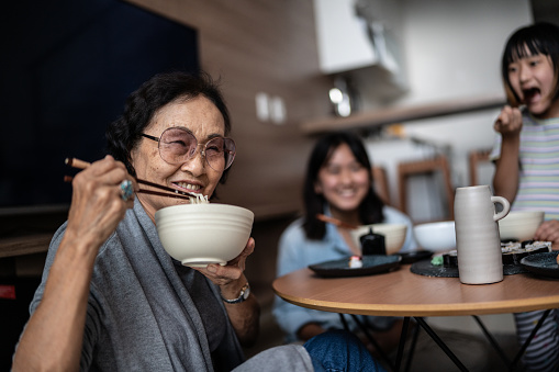 Portrait of a happy senior woman eating japanese food with family at home