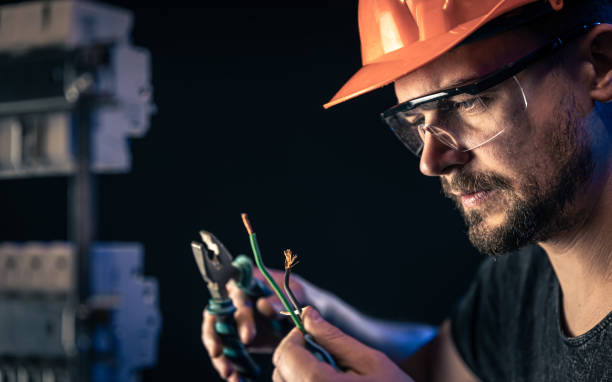 A male electrician works in a switchboard with an electrical connecting cable. A male electrician in a protective helmet works in a switchboard with an electrical connecting cable. electrician stock pictures, royalty-free photos & images