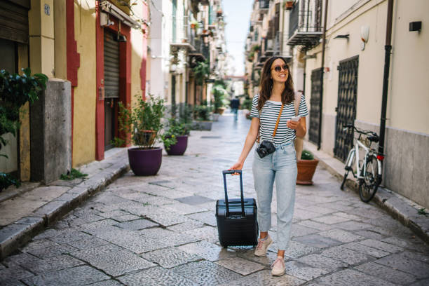 istock Young woman pulls suitcase down cobblestone street 1369213256