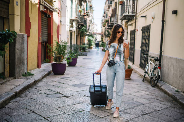 Young woman pulls suitcase down cobblestone street stock photo