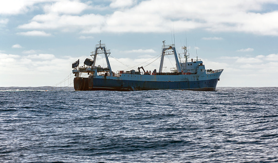 Commercial fishing trawler is fishing for marine fish and seafood in oceanic waters. Large fishing vessel lifts  trawl tackle in the southern waters of the Atlantic.
