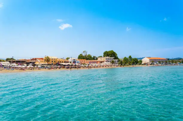 Photo of Roda tourist town on Corfu island, Greece. Beautiful village on seashore with colorful houses, beach bars and restaurants, sun beds, umbrellas and turquoise water. Popular summer vacation destination