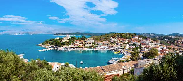 Panorama of Kassiopi town on Corfu island, Greece. Picturesque fishing village on rugged seashore with colorful houses, luxury villas and turquoise water. Popular tourist destination.