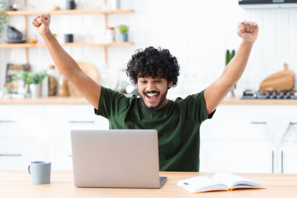 istock Happy young indian man looking at computer screen making yes gesture, happy with great news, received a nice message in the mail, celebrates success 1369214084