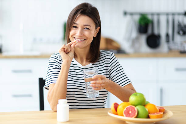 Young beautiful smiling caucasian woman holding vitamin pill and glass of water, looking at the camera and smiles friendly. Healthy lifestyle, healthy diet nutrition concep stock photo
