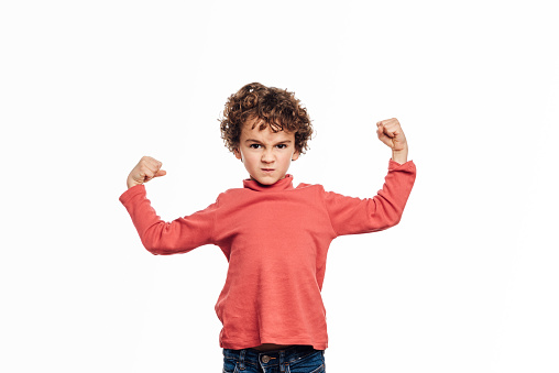 Angry young boy raising both arms with clenched fists to show strength while standing over an isolated background.