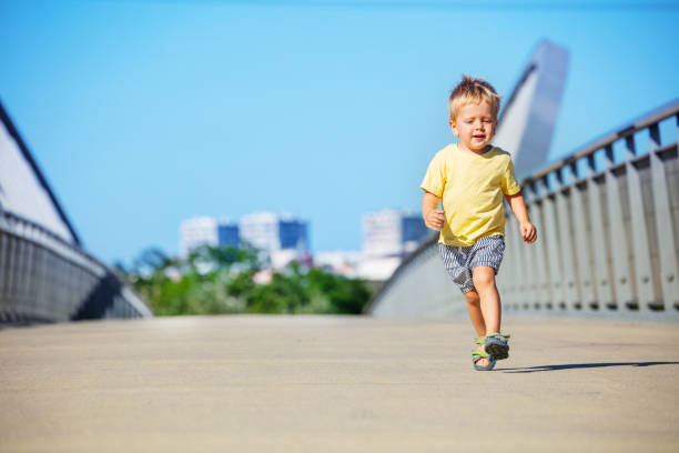 Cute blond toddler boy run on the pedestrian bridge smiling