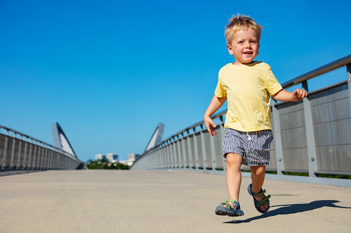 Little blond toddler boy run on the pedestrian bridge smiling