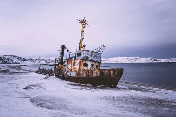 Photo of An old abandoned ship on the shore of the Barents Sea in the Arctic Ocean. The village of Teriberka Kola peninsula. The destroyed economy and industry of Russia concept