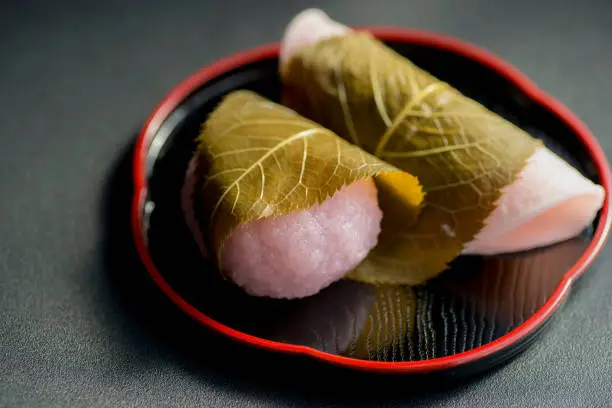 Close-up of two kinds of "sakura mochi," Japanese sweets served on a black plate.