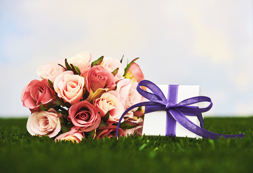 Rose bouquet on grass with gift box and space for copy. Mother's Day background