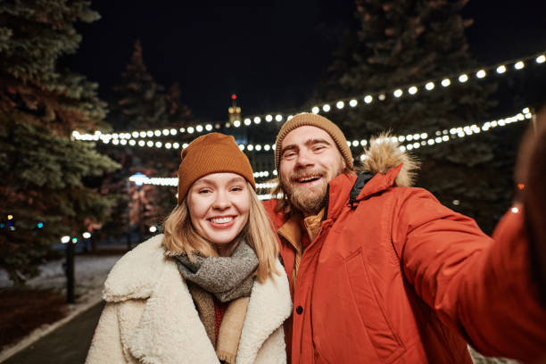 istock Horizontal medium shot joyful  young couple spending winter evening outdoors having fun taking selfies on smartphone camera 1369245548