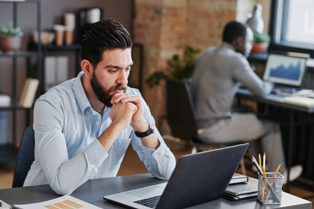 istock Horizontal medium shot of young Middle Eastern man working on office sitting at desk looking at computer screen thinking about something 1369248590