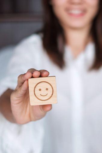 Happy Woman holding smile emotion face block. Customer choose Emoticon for user reviews. Service rating, mental health, positive thinking, satisfaction, evaluation and feedback concept