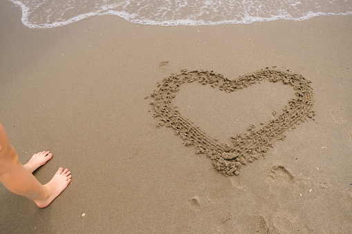 Heart drawn on a sandy beach. Children's bare feet. Sea waves.