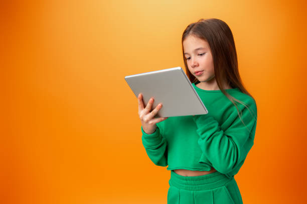istock Beautiful teen girl using digital tablet over orange studio background 1369264637