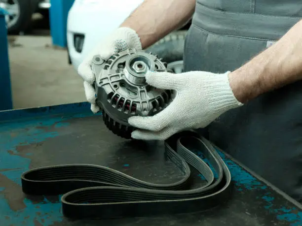 The mechanic checks the generator and the drive belt of the internal combustion engine units before installation during the repair of the car in the service center