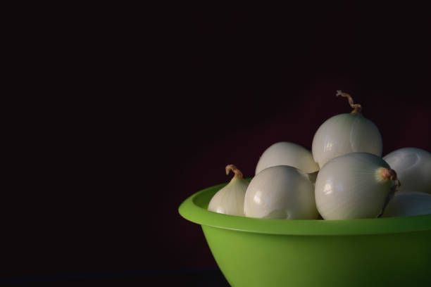 Peeled onions in a green colander on black background. Copy space. Close -up