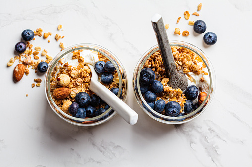 Granola with nuts, yogurt and berries in a jar, top view. Breakfast parfait with muesli, yoghurt and blueberries, white background.
