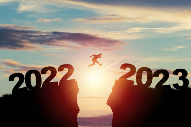 bienvenido feliz navidad y feliz año nuevo en 2023, silhouette man saltando del acantilado de 2022 al acantilado de 2023 con cielo nublado y luz solar. - enero fotografías e imágenes de stock