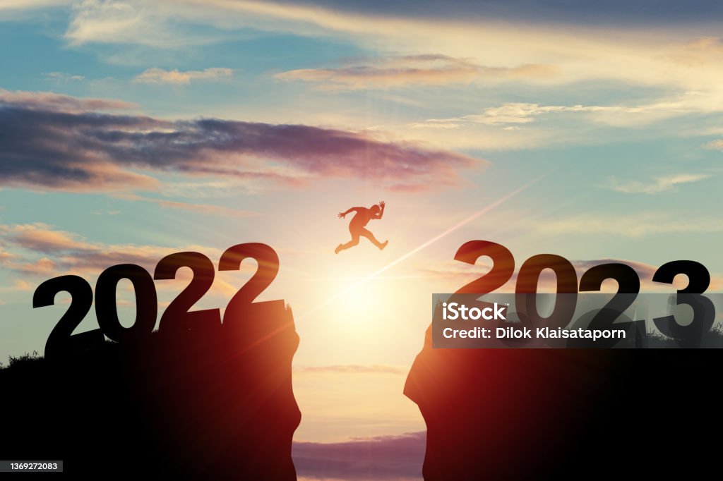 Welcome merry Christmas and happy new year in 2023,Silhouette Man jumping from 2022 cliff to 2023 cliff with cloud sky and sunlight. 2023 Stock Photo