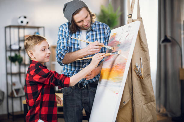 istock Father helping son drawing with brush on canvas 1369272245