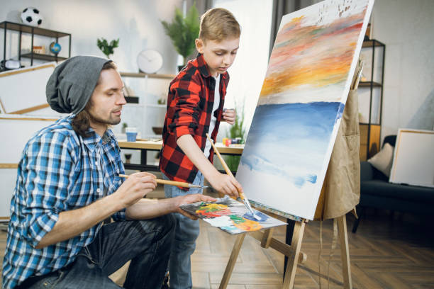 istock Man teaching little boy painting on canvas 1369272996