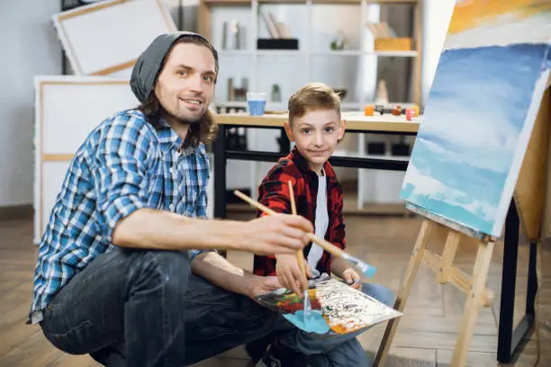 Photo of Teacher and student painting together on easel at studio
