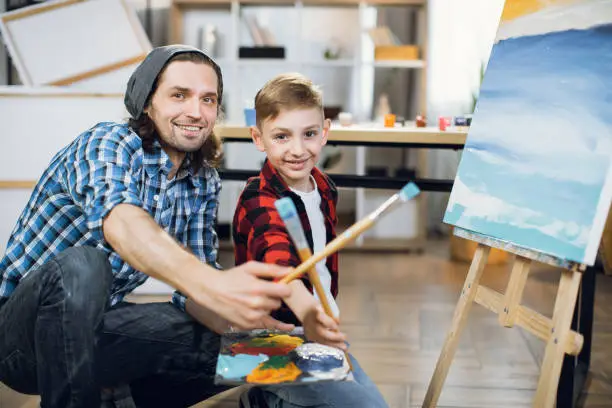 Photo of Teacher and student painting together on easel at studio