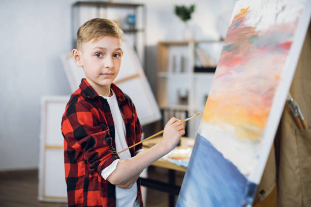 istock Talented boy drawing with brush and paints on easel 1369273172