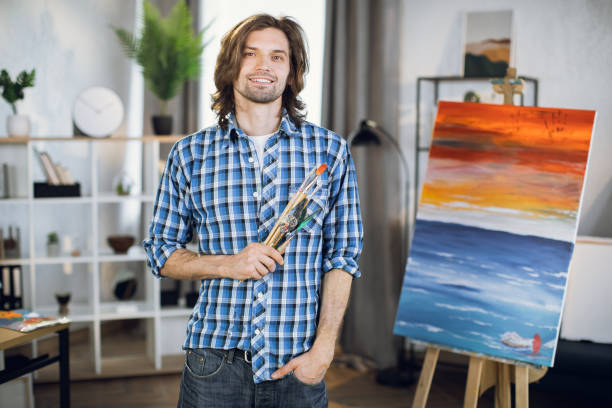 istock Positive artist with brushes in hands posing near easel 1369275000