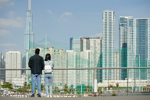 Young couple standing on bridge and enjoying cityscane, view from the back