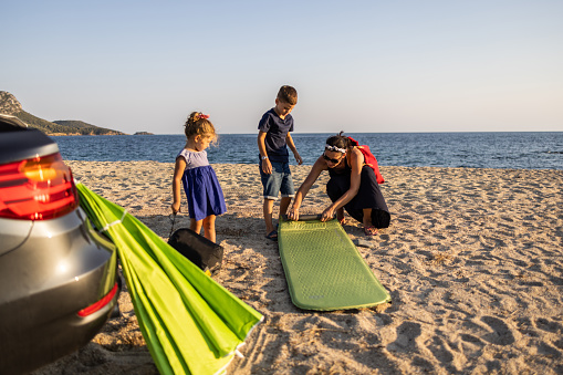 Young mother with two kids packing beach mat after day on beach